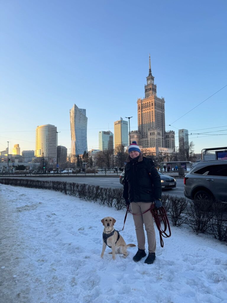 Mężczyzna z psem labradorem biszkoptowym na tle Pałacu Kultury w Warszawie